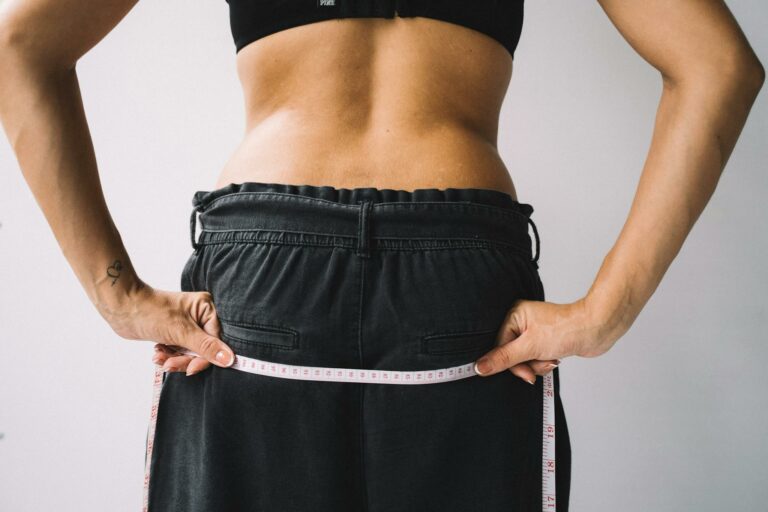 A person measuring their waist with a tape measure, symbolizing fitness goals.