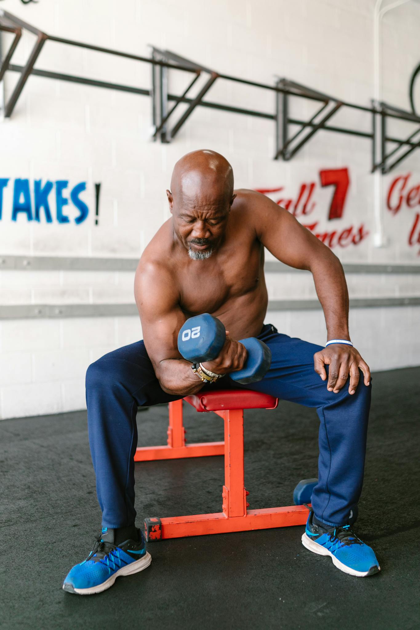 A senior man exercises bicep curls with dumbbells inside a gym.