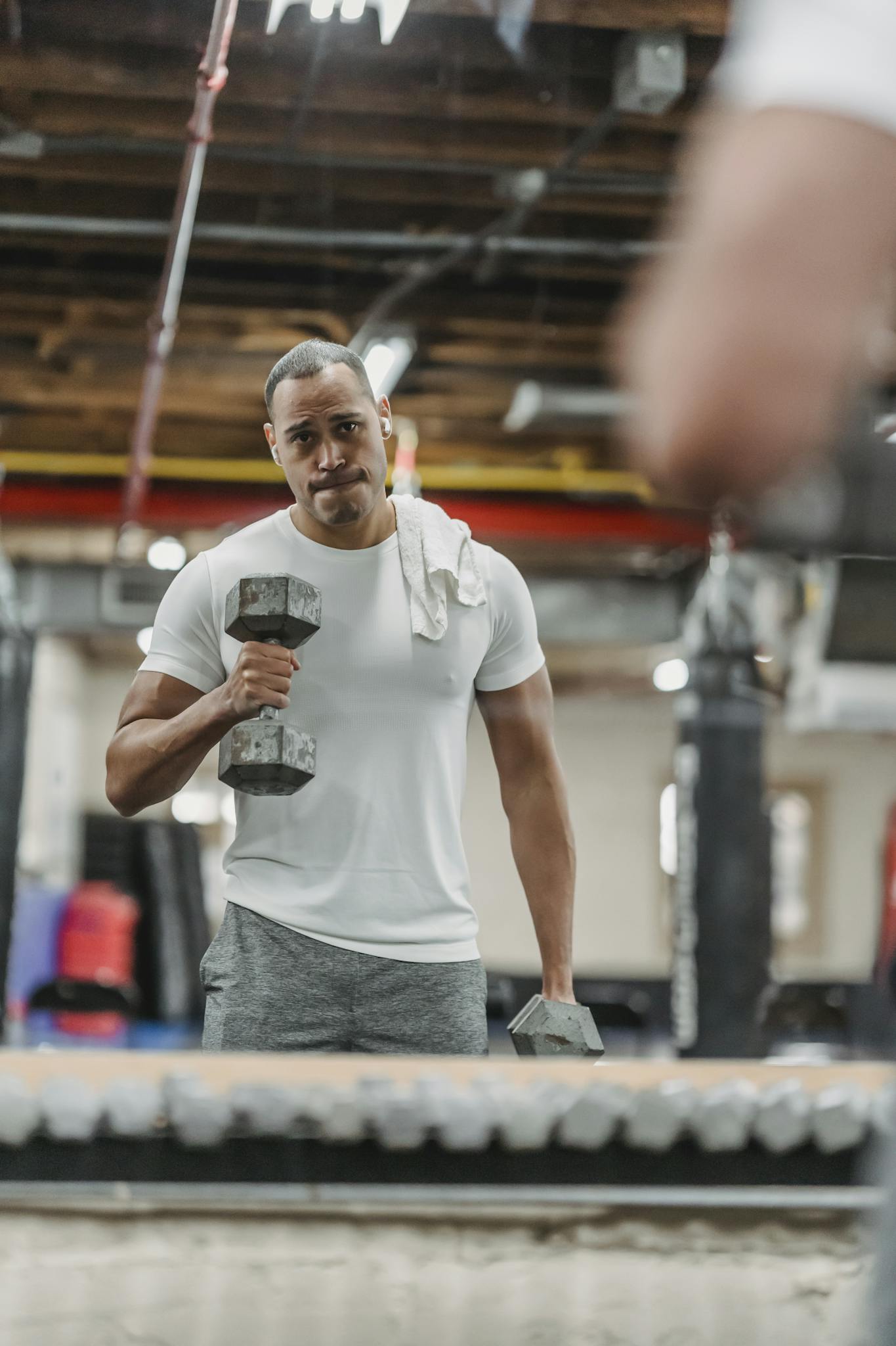 An athletic African American man lifting dumbbells with reflection in the gym mirror.